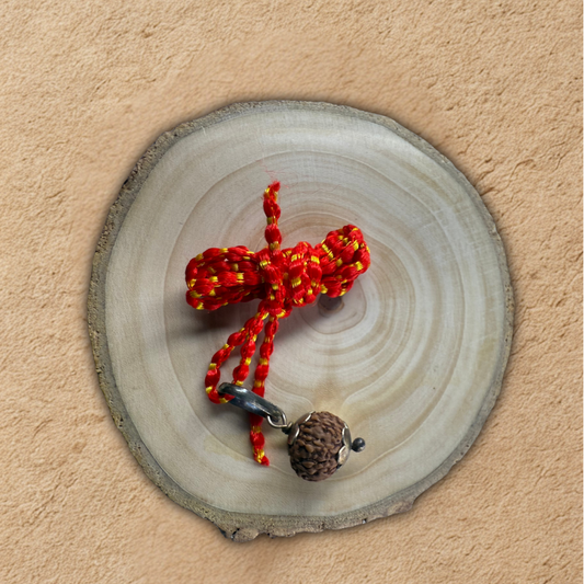 Red and yellow braided keychain with a brown bead on a wooden disc against a beige background