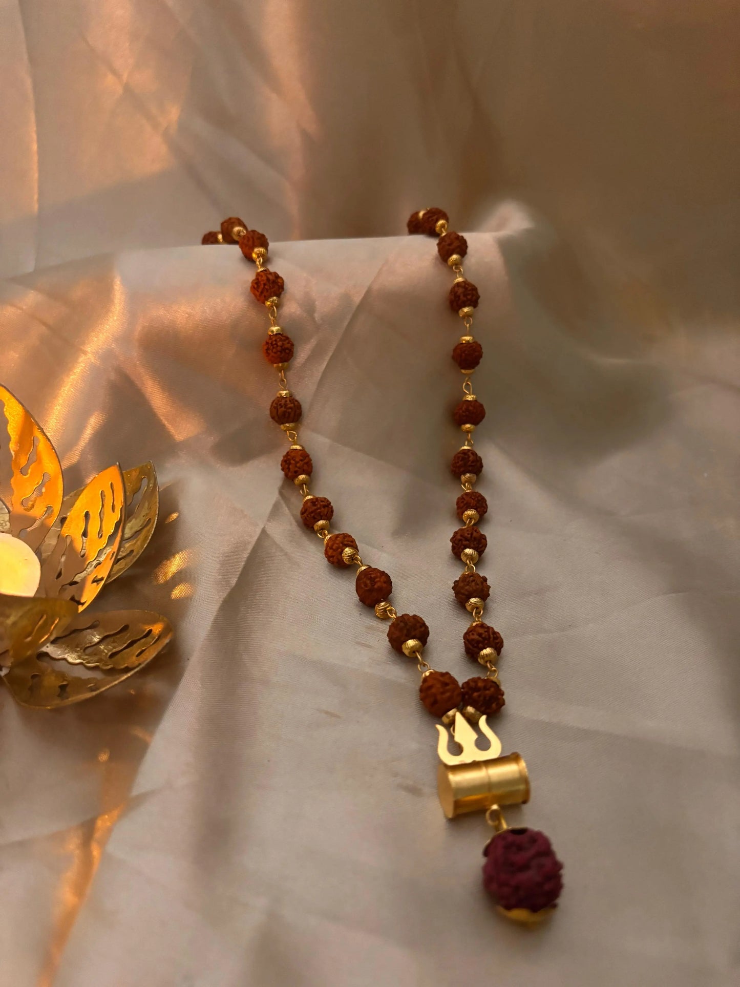 Beaded necklace with gold and red beads on a light fabric background Rudraksha Mala
