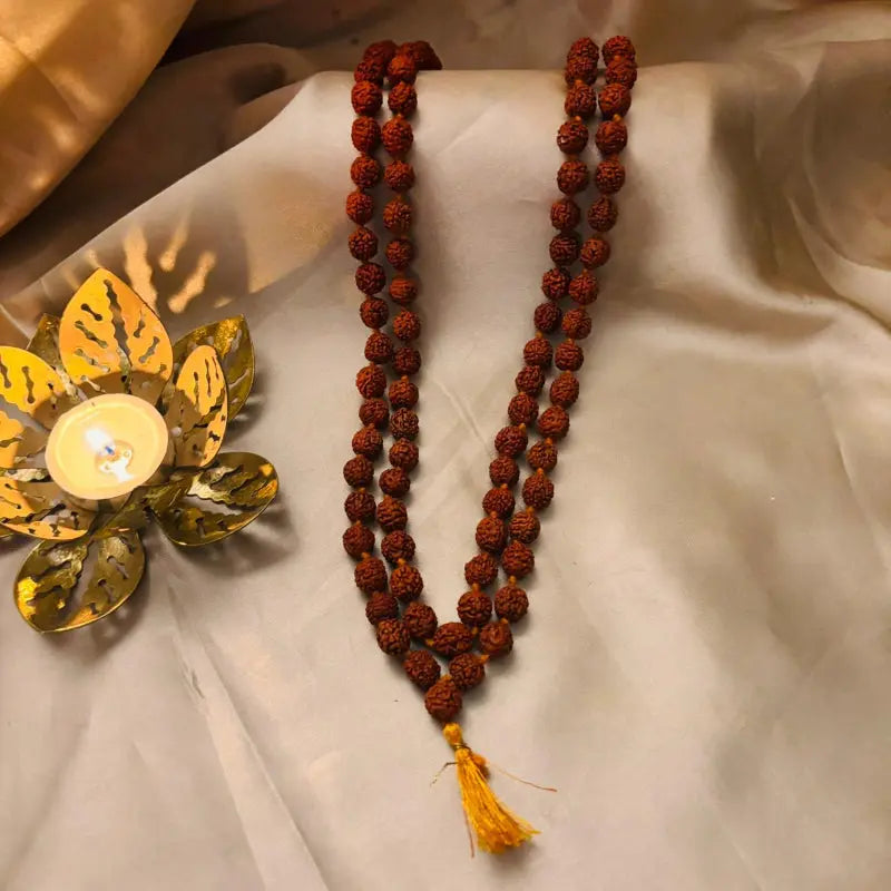 Meditative setup with a rosary, candle, and decorative leaf on a textured surface